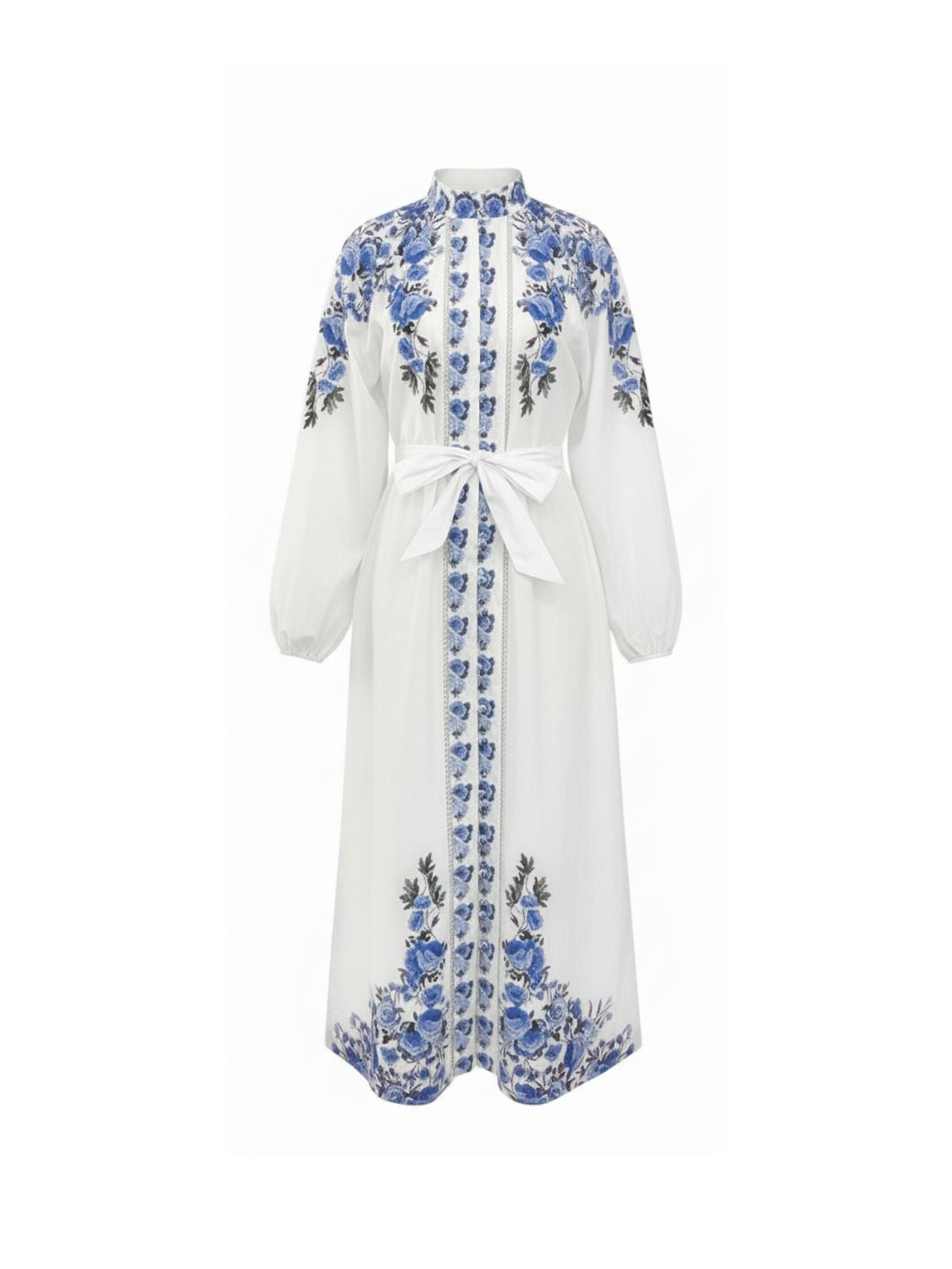 Robe Eloise Elyth Édition : robe longue blanche en lin et coton à col montant, ornée de riches broderies florales bleues sur les épaules et les ourlets, dotée d'un boutonnage frontal complet, de manches bouffantes et d'une ceinture nœud à la taille.
